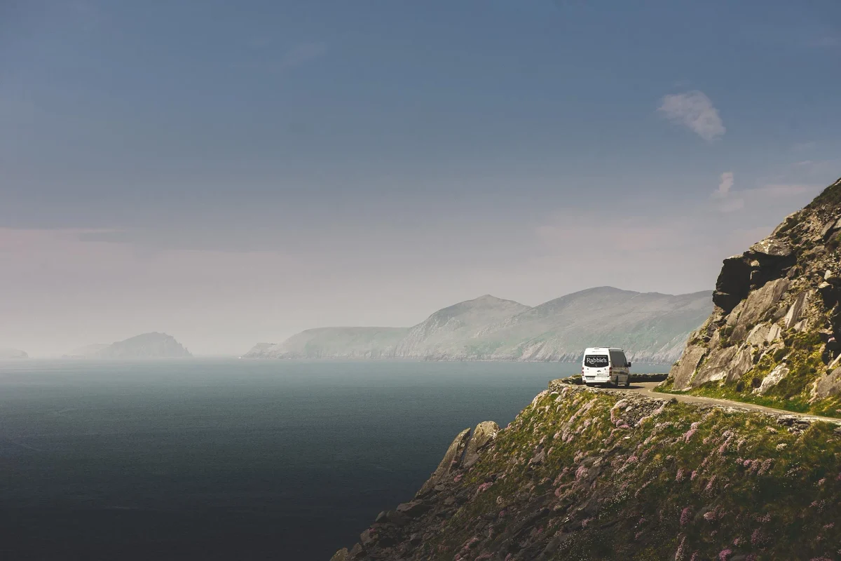 A Rabbie's tour bus on a winding road above the Scottish coastline